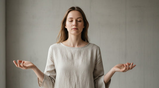 A person standing with eyes closed and hands relaxed, practicing mindfulness and sensory awareness in a calm minimalist space.