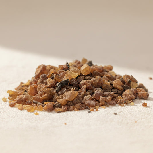 Close-up of sustainably harvested Somali myrrh resin, small amber and brown granules resting on a soft neutral fabric surface.